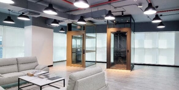 Cibes Abu Dhabi showroom interior with two demo home lifts in glass shafts and lounge seating.