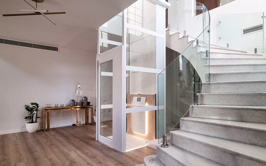 Cibes Air home elevator with white panoramic shaft installed beside a marble staircase in a premium villa in Mirdif, Dubai.