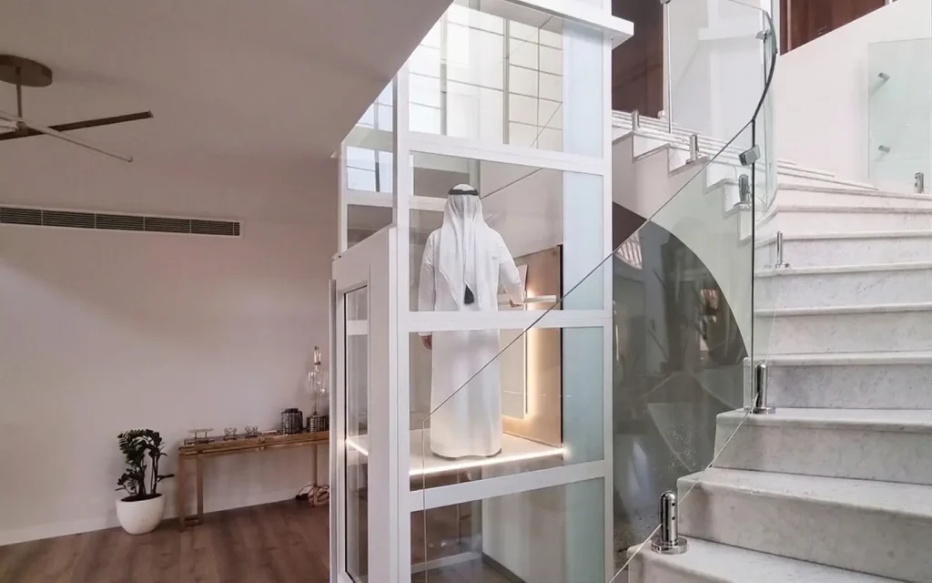 Homeowner using a glass platform lift installed beside a staircase in a UAE villa.